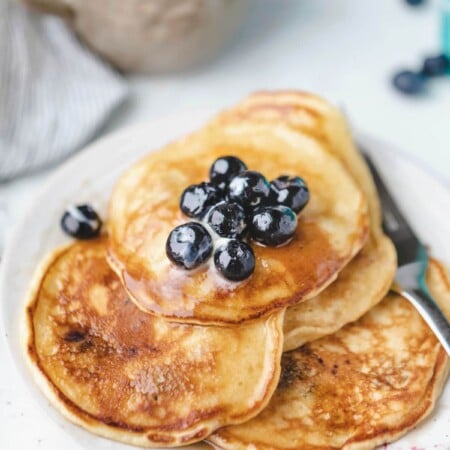Plate of blueberry pancakes topped with butter and fresh blueberries.