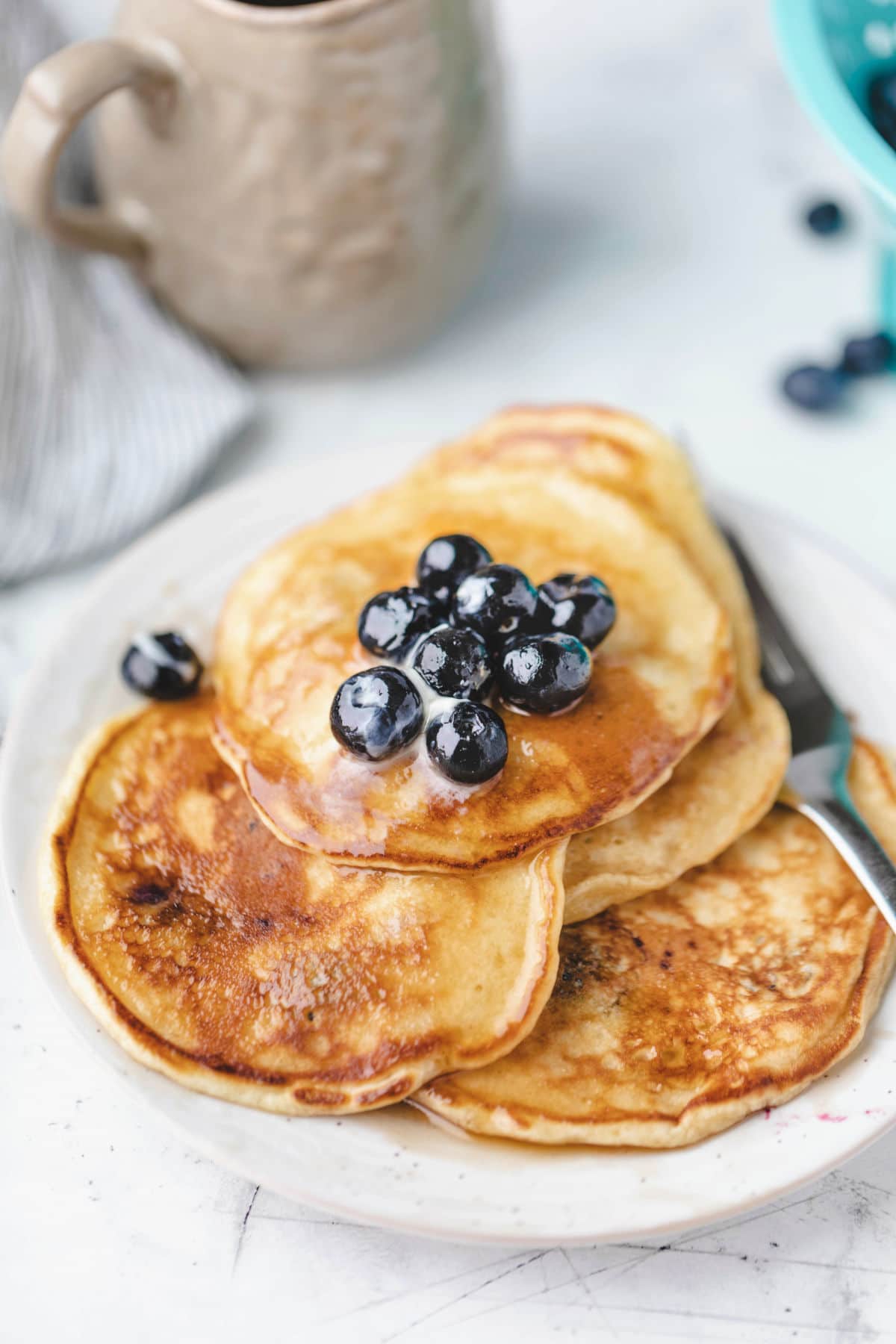 Plate of blueberry pancakes topped with butter and fresh blueberries.