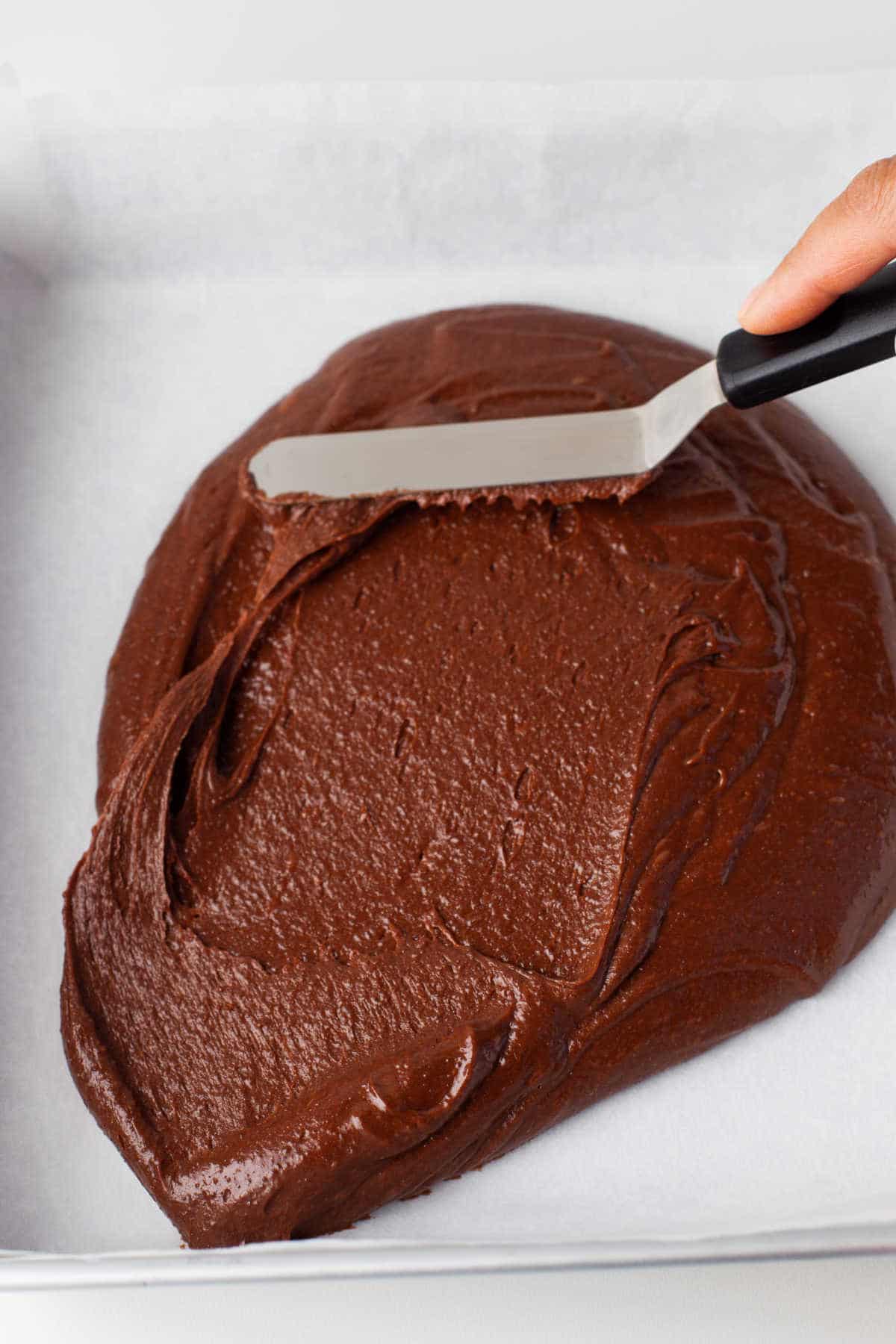 An offset spatula spreading brownie batter in a pan.