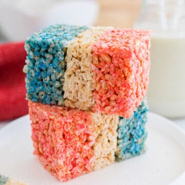 Two red white and blue rice krispies treats stack on each other on a white plate.