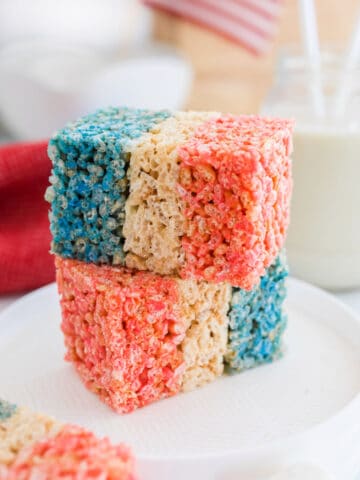 Two red white and blue rice krispies treats stack on each other on a white plate.