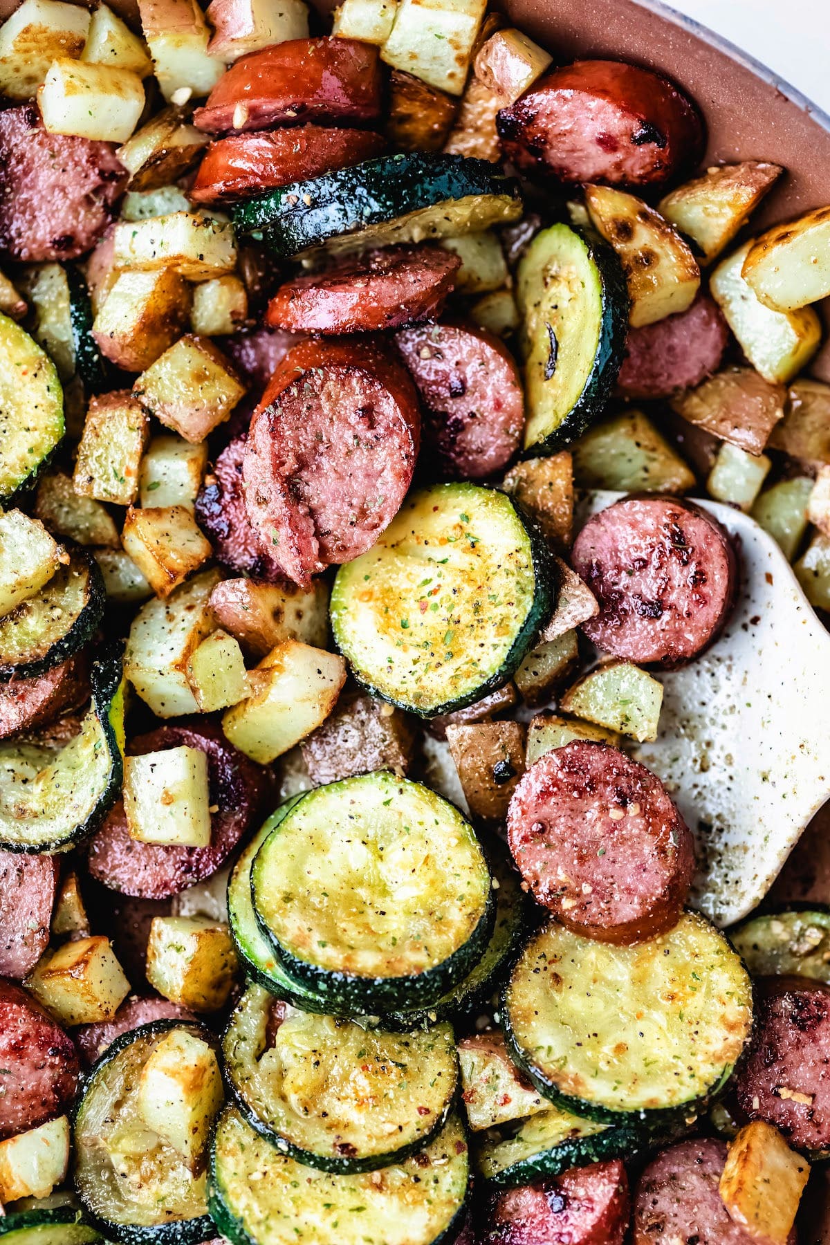 A tan spatula scooping up kielbasa zucchini and potatoes.