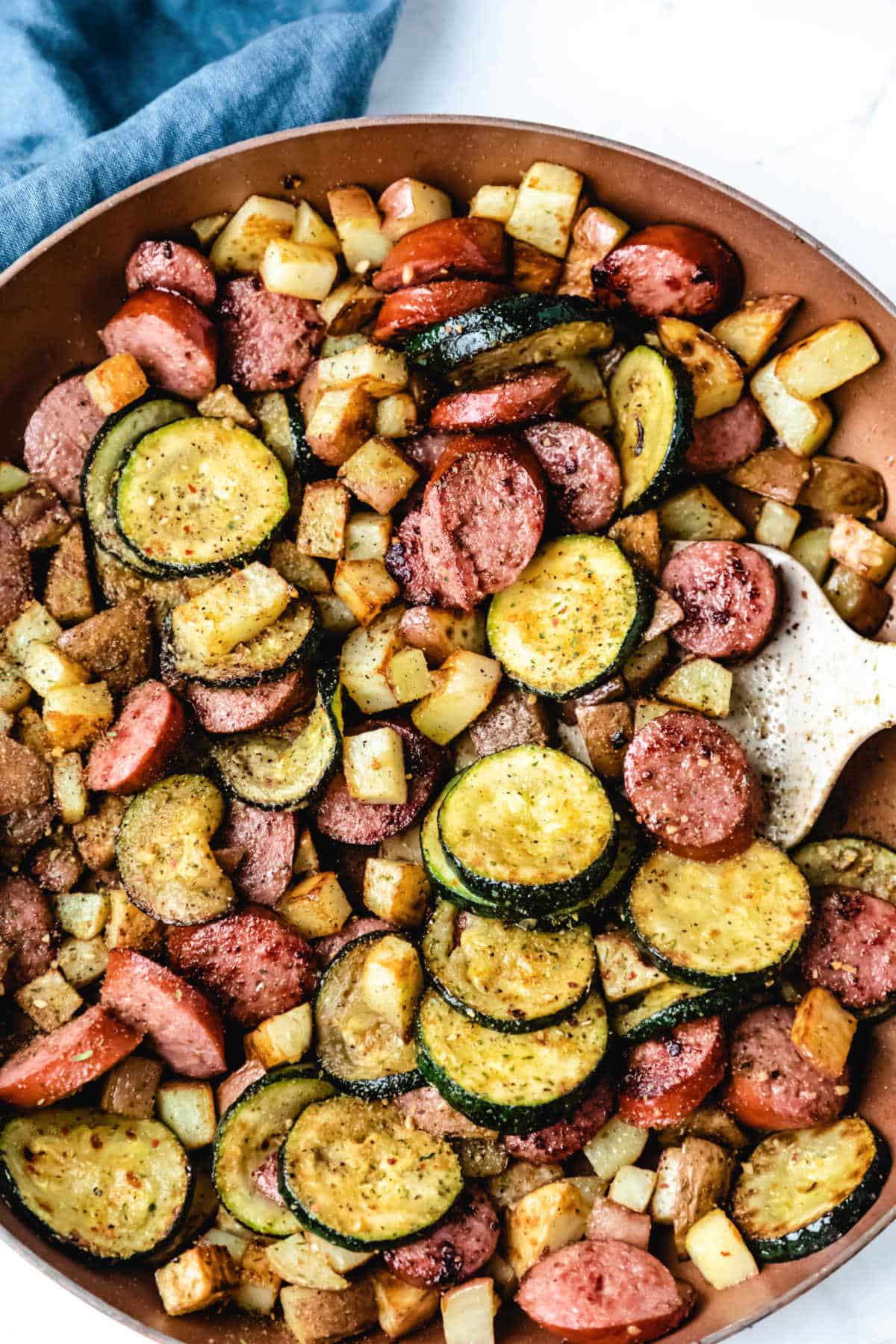 Kielbasa zucchini and potato skillet next to a blue linen. 