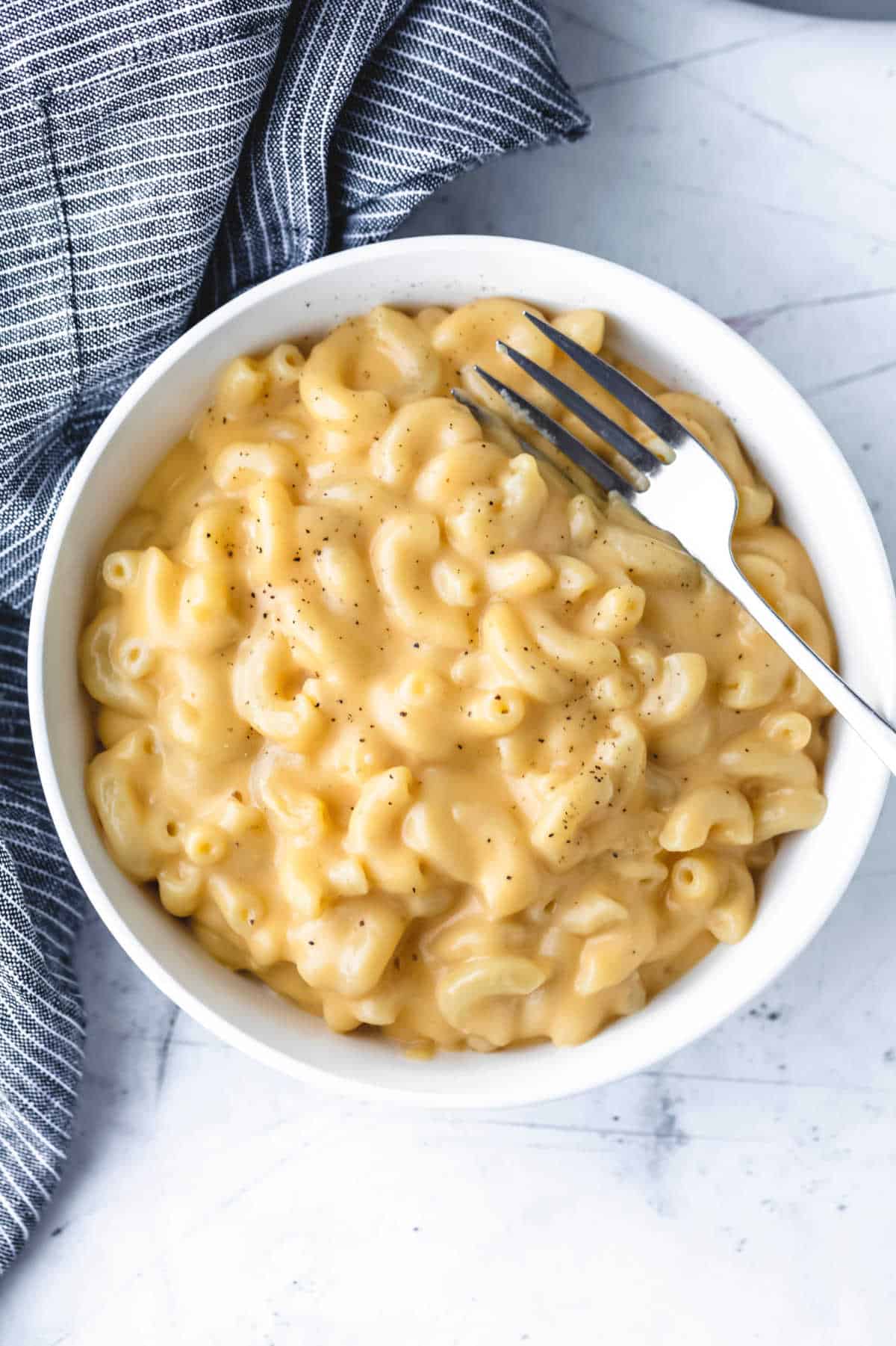 A fork in a bowl of macaroni and cheese. 