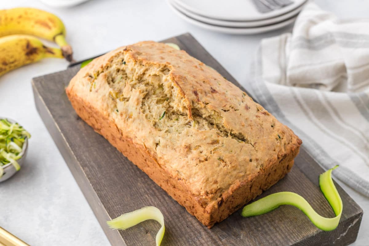 Loaf of zucchini banana bread next to bananas and shredded zucchini.