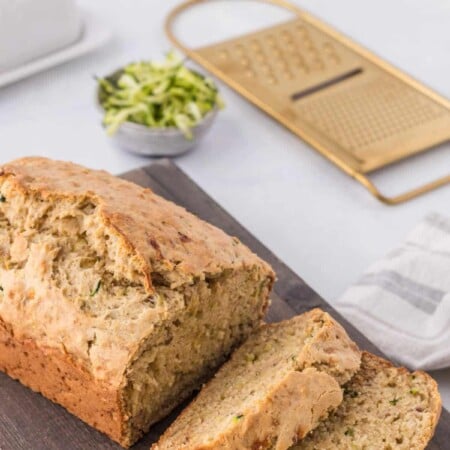 A loaf of banana zucchini bread on a cutting board with two slices cut.