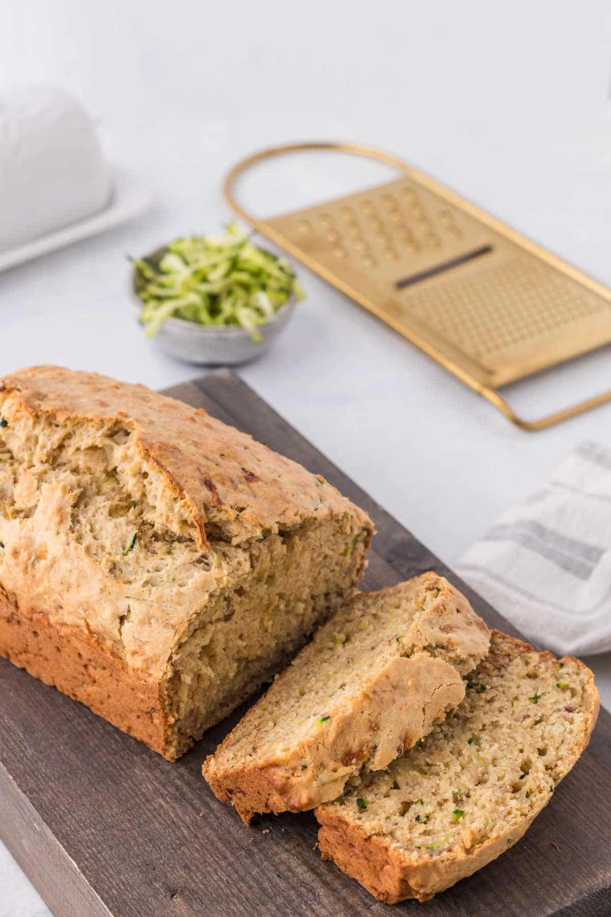 A loaf of banana zucchini bread on a cutting board with two slices cut. 