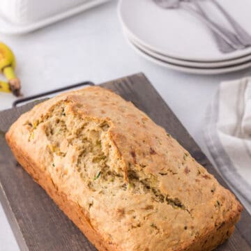 Loaf of zucchini banana bread on a wooden cutting board.