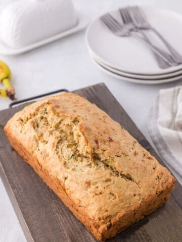 Loaf of zucchini banana bread on a wooden cutting board.