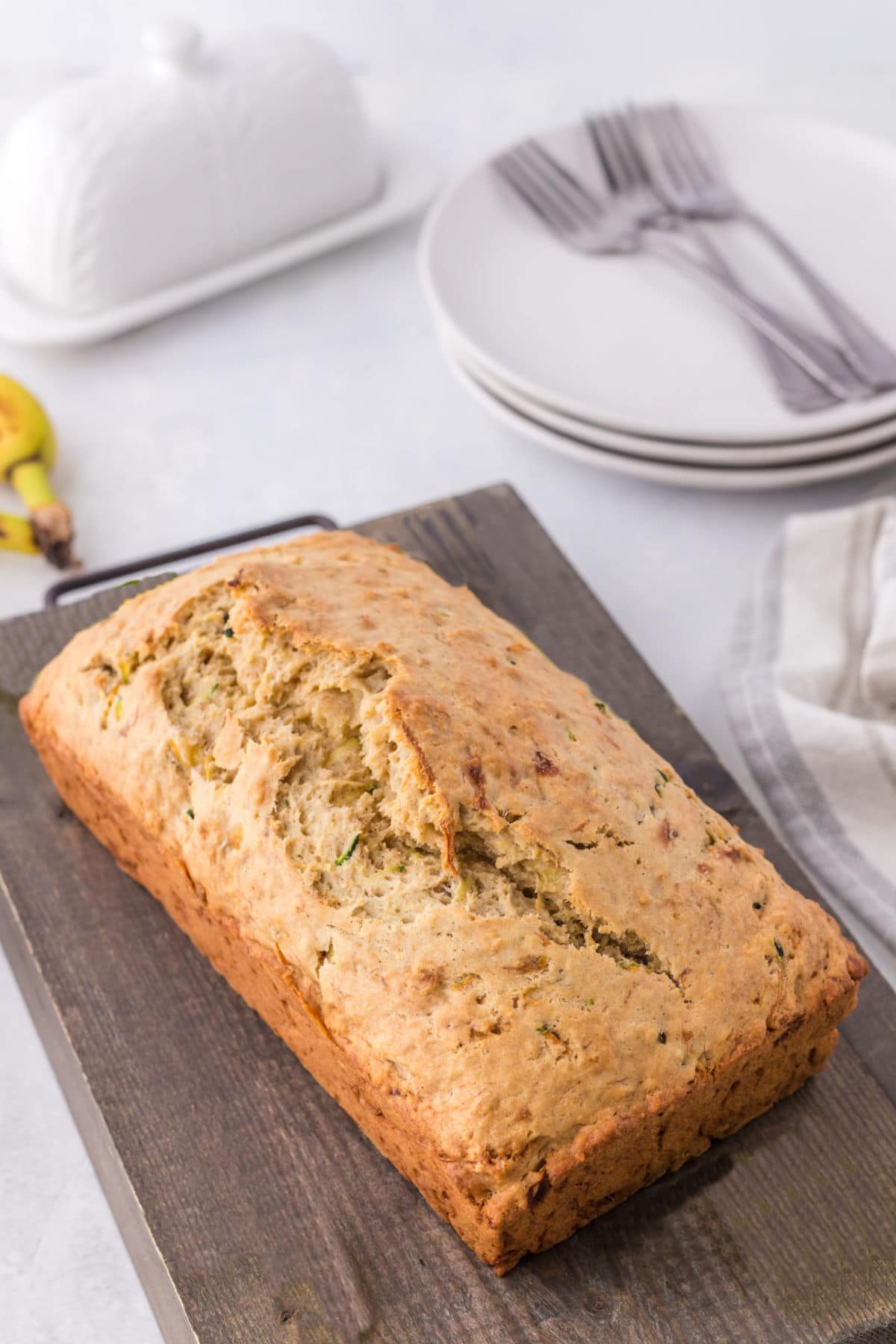 Loaf of zucchini banana bread on a wooden cutting board. 