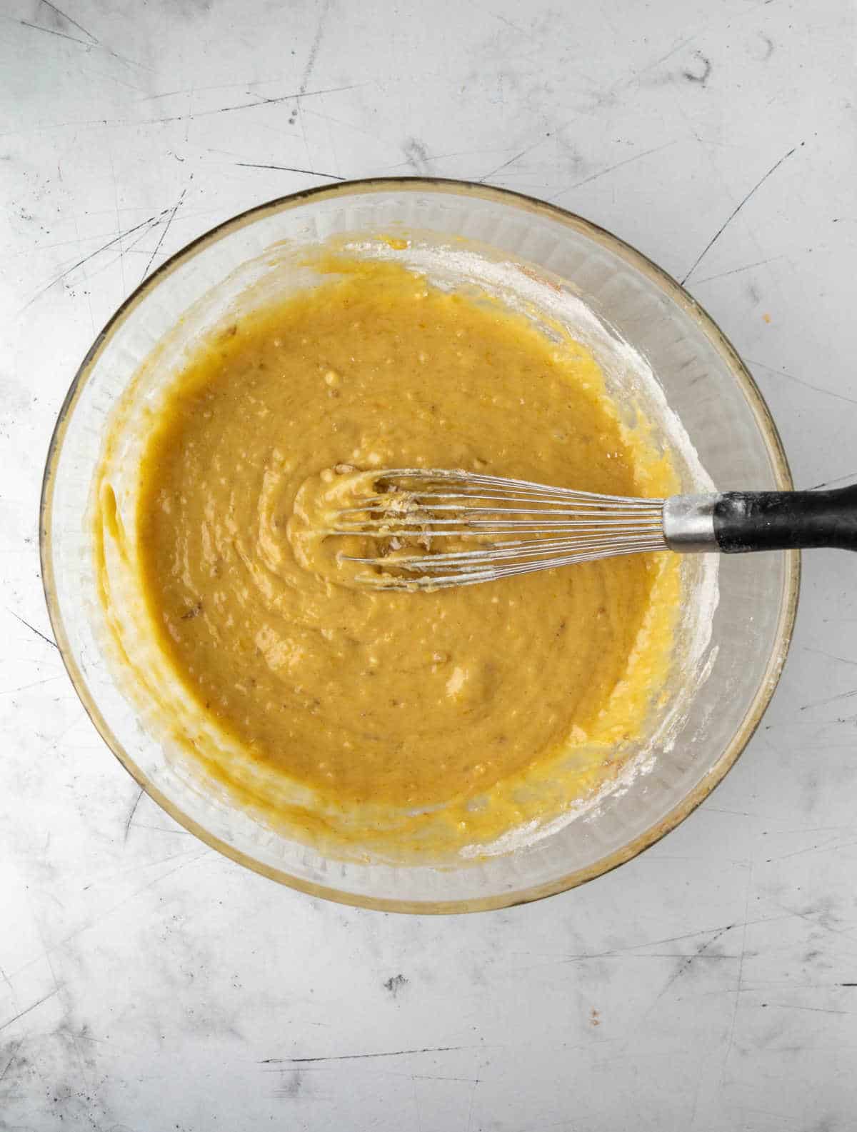 Wet and dry ingredients for banana zucchini bread in a glass mixing bowl.
