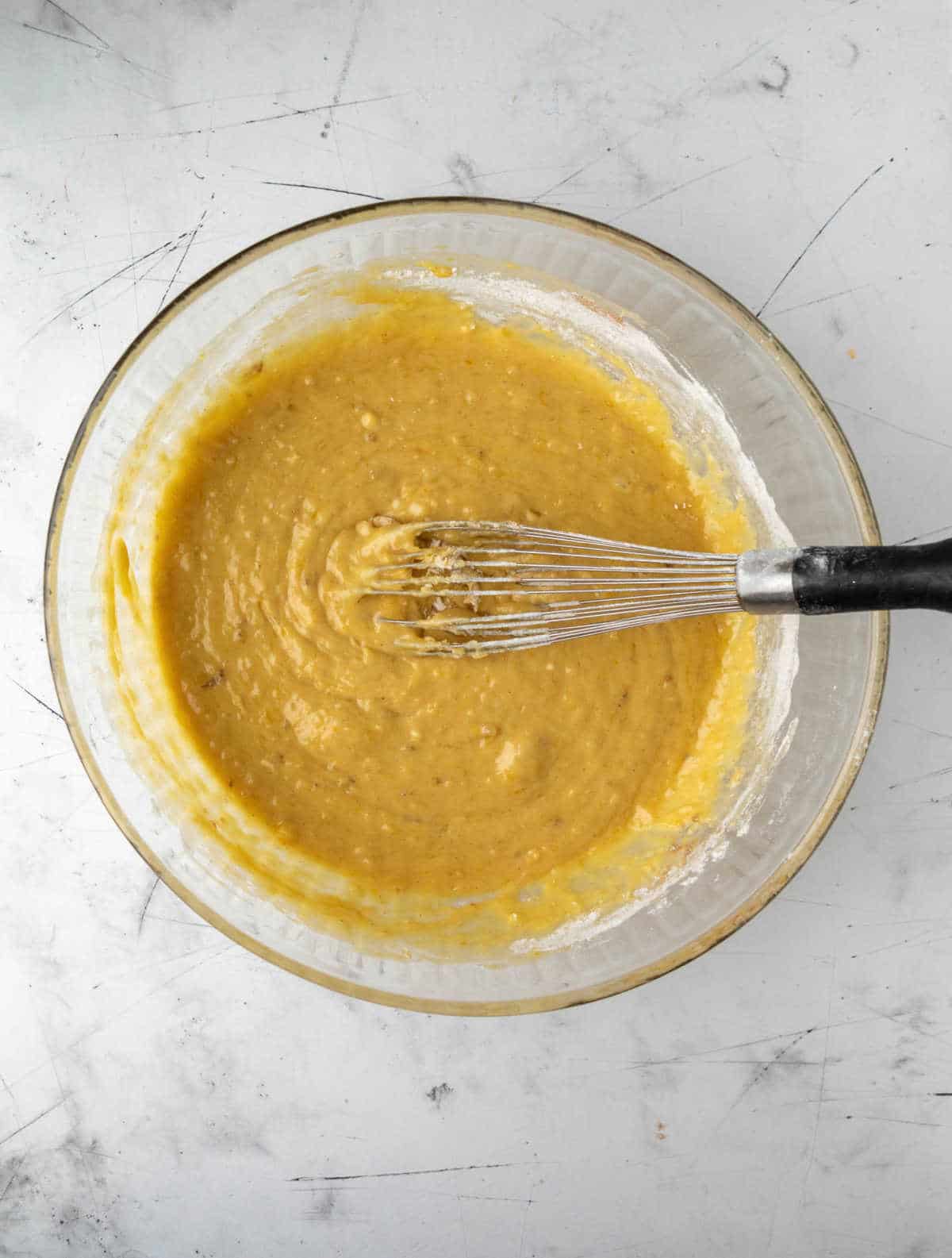 Wet and dry ingredients for banana zucchini bread in a glass mixing bowl. 