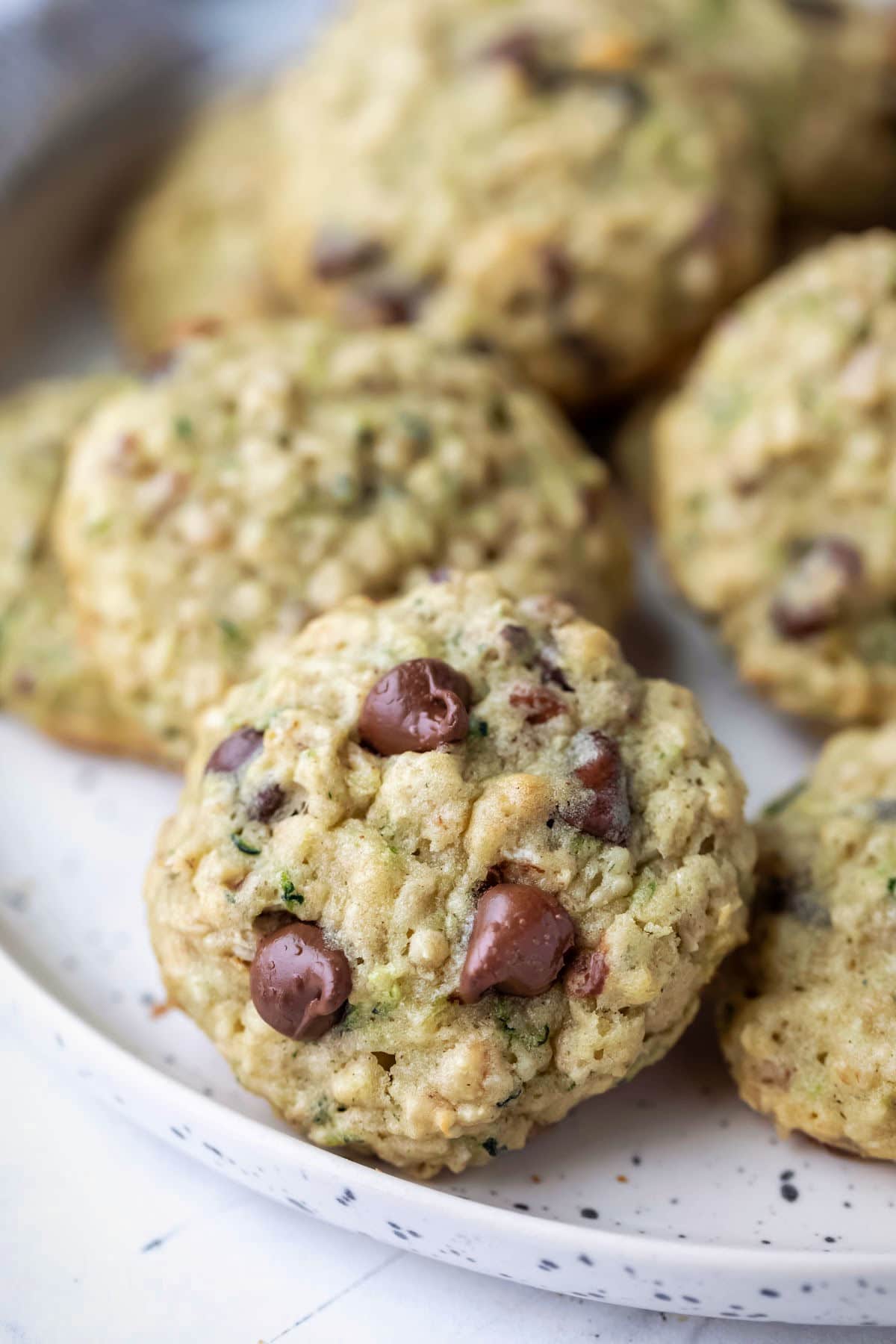 A plate of zucchini chocolate chip cookies with an upright cookie in the front.