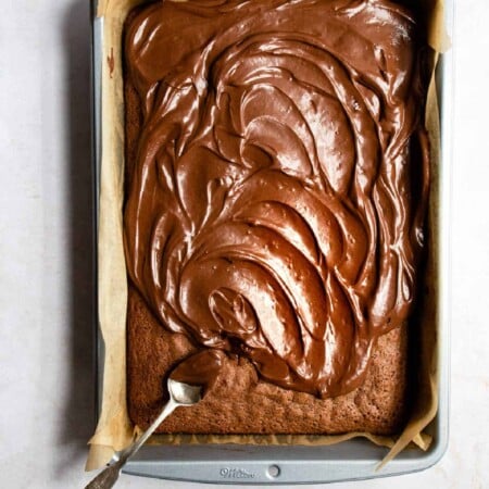 A spoon spreading chocolate frosting onto brownies.