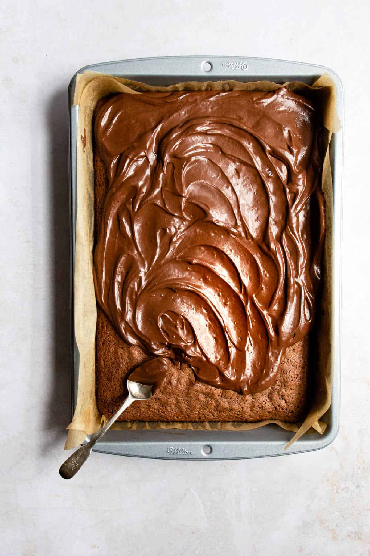 A spoon spreading chocolate frosting onto brownies. 