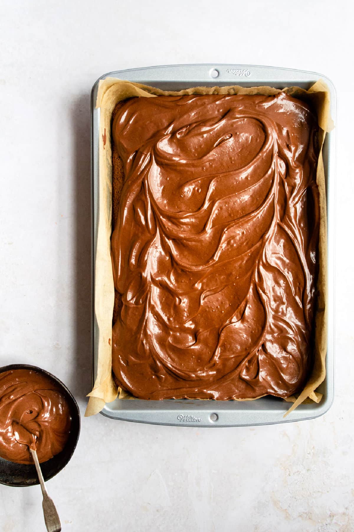 A pan of frosted brownies next to a bowl of frosting.