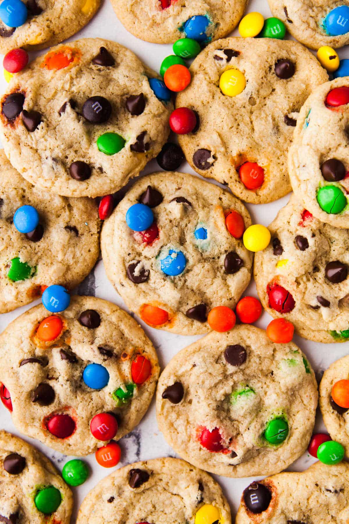 Bakery Style M&M Chocolate Chip Cookies Overlapping M&M cookies with M&Ms scattered around.