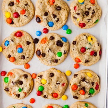 A dozen M&M cookies on a piece of parchment paper.