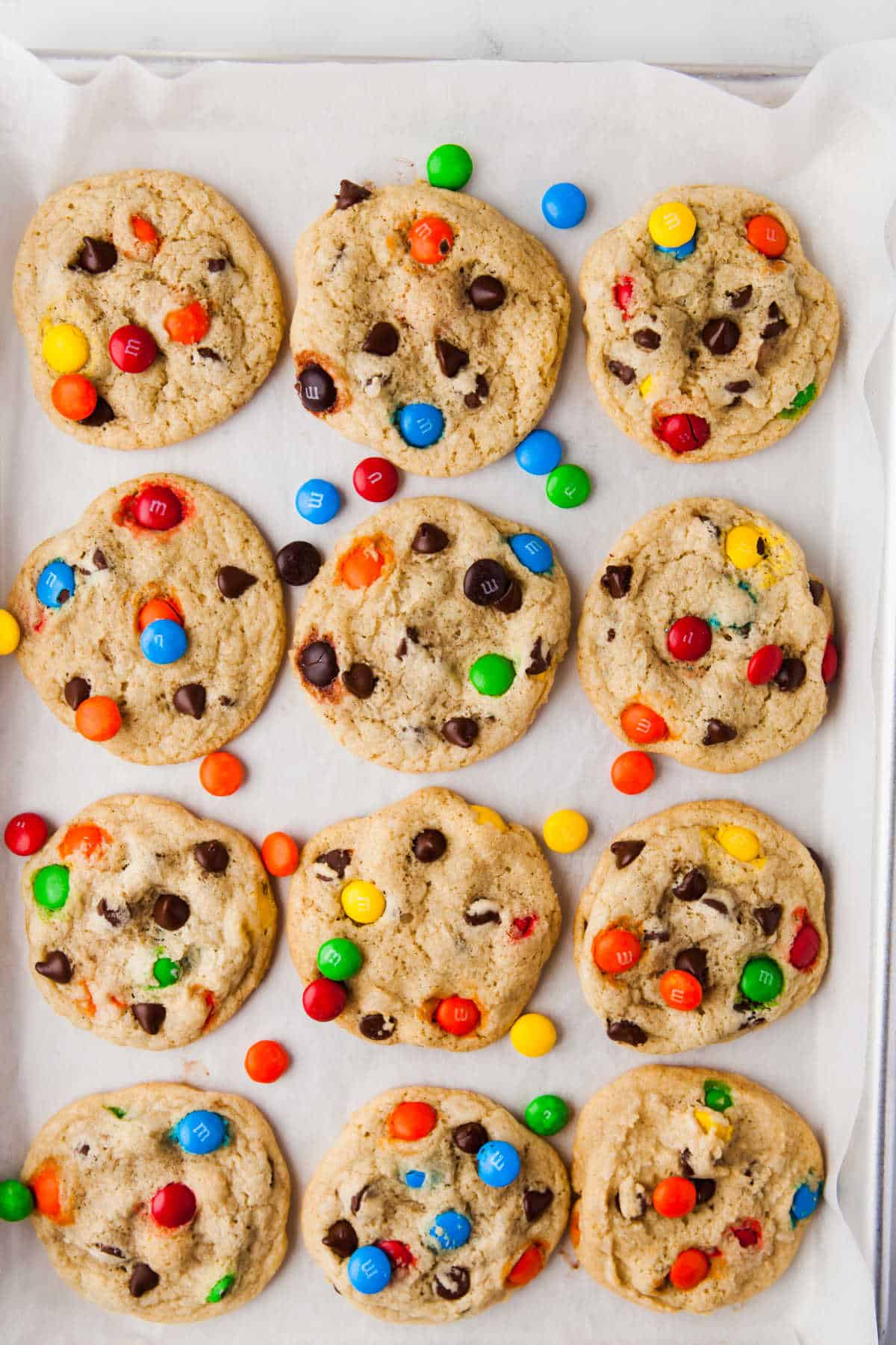 A dozen M&M cookies on a piece of parchment paper.