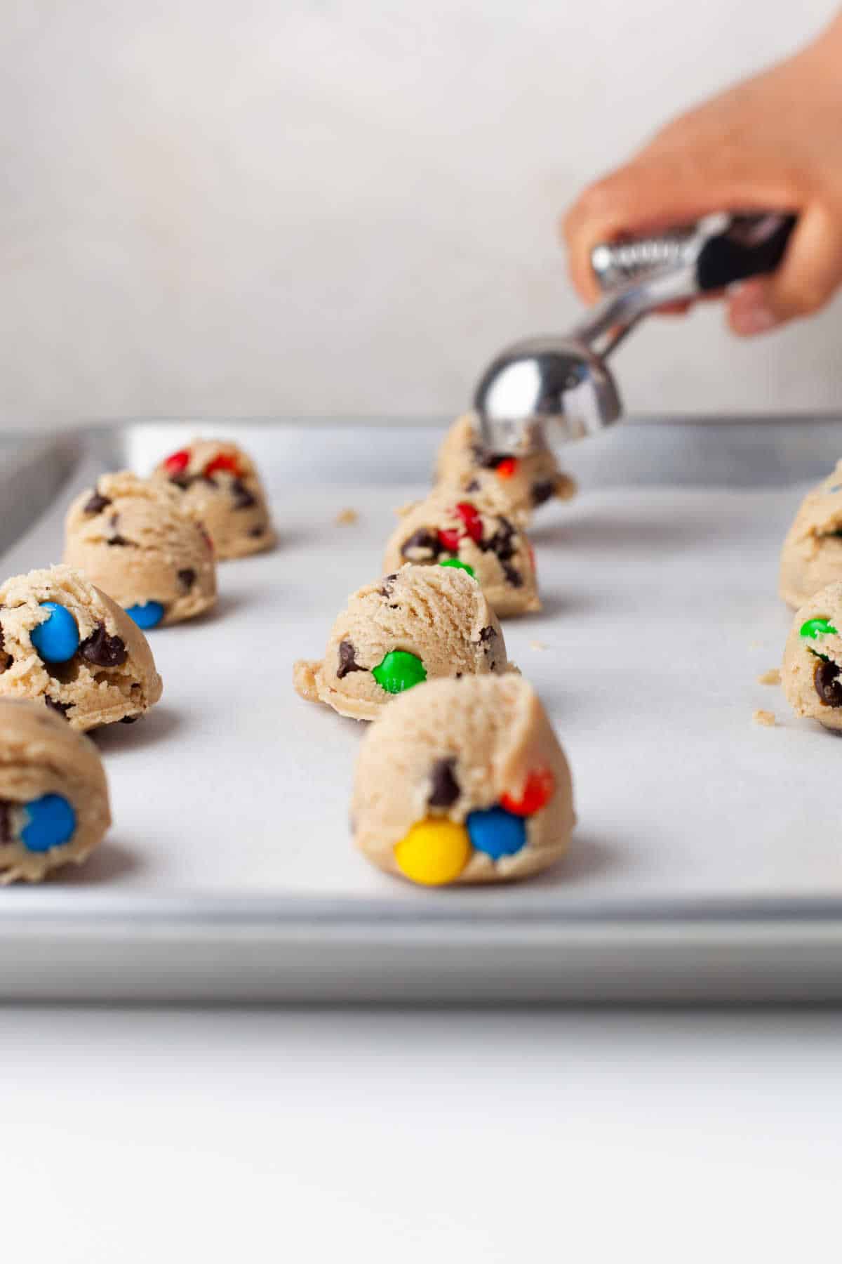 A cookie scoop dropping scoops of cookie dough onto a cookie sheet. 