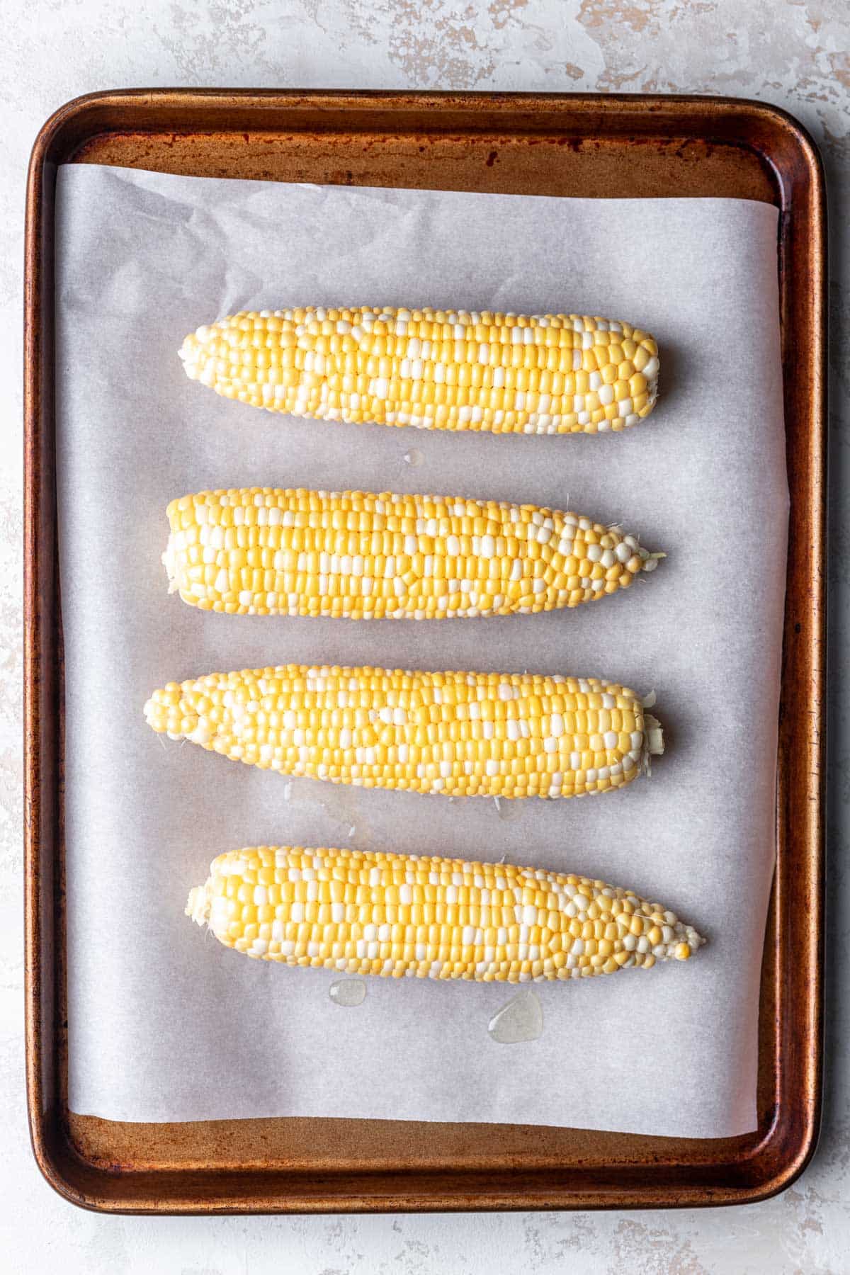 Four ears of corn on a baking sheet. 