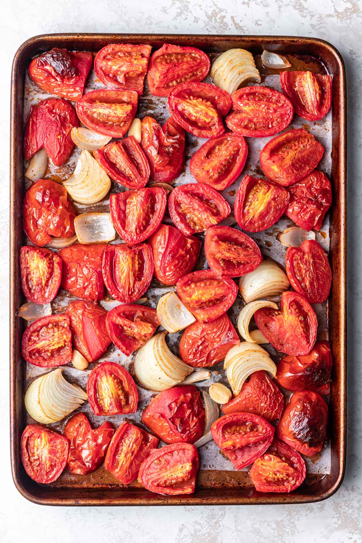 Roasted tomatoes onion and garlic on a sheet pan. 