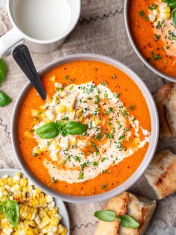 A bowl of roasted tomato and corn soup next to a dish of cream.