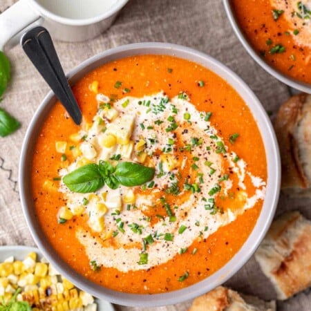 A bowl of roasted tomato and corn soup next to a dish of cream.