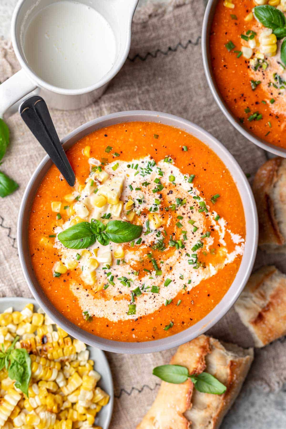 A bowl of roasted tomato and corn soup next to a dish of cream. 