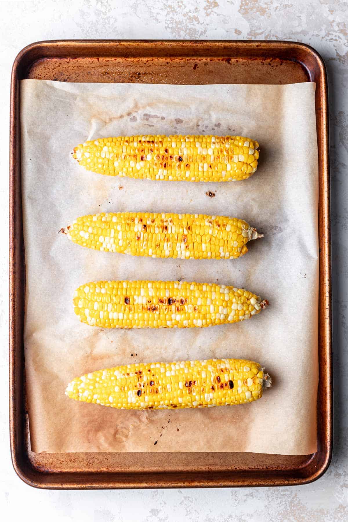 Four ears of roast corn on a baking sheet. 