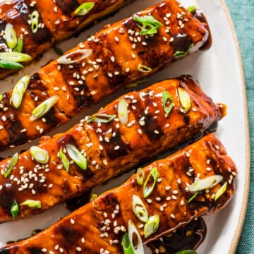 Four pieces of grilled teriyaki salmon on a white platter.