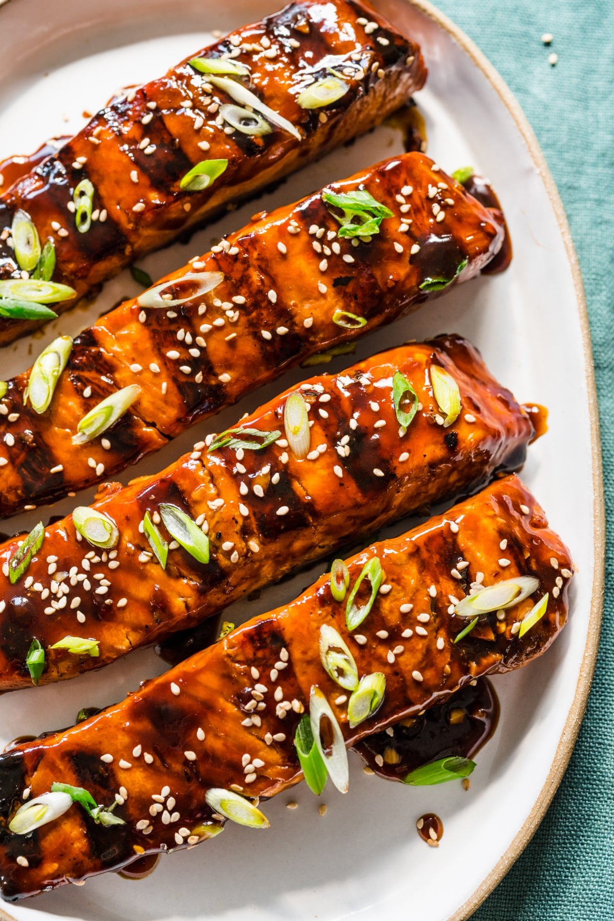 Four pieces of grilled teriyaki salmon on a white platter. 