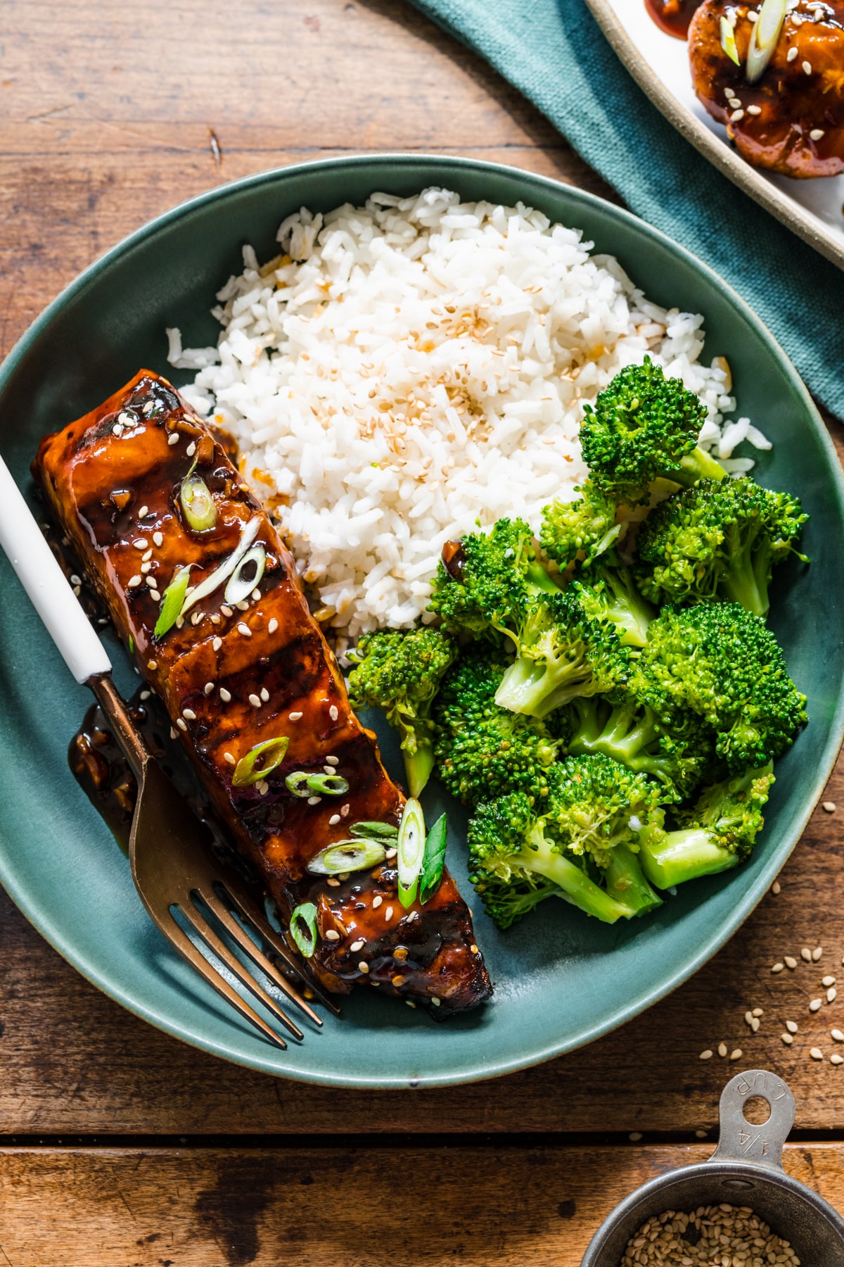 A blue plate with grilled teriyaki salmon next to rice and broccoli.