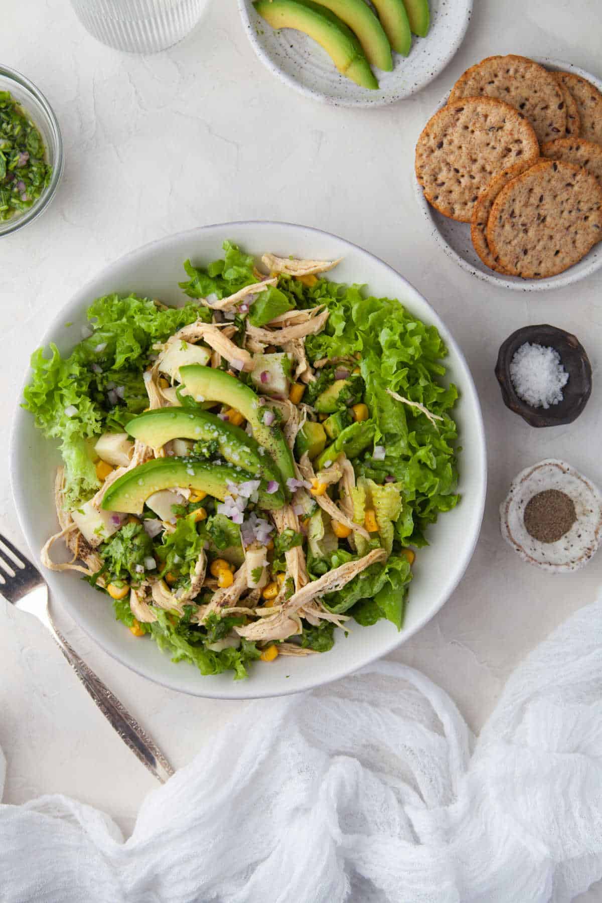 Plate of avocado chicken salad next to a plate of sliced avocados. 