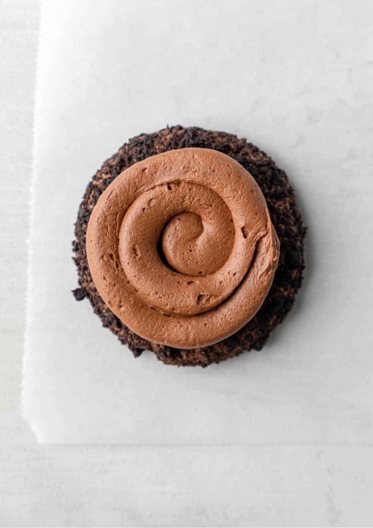 A chocolate frosted dirt cookie on a piece of white parchment paper. 