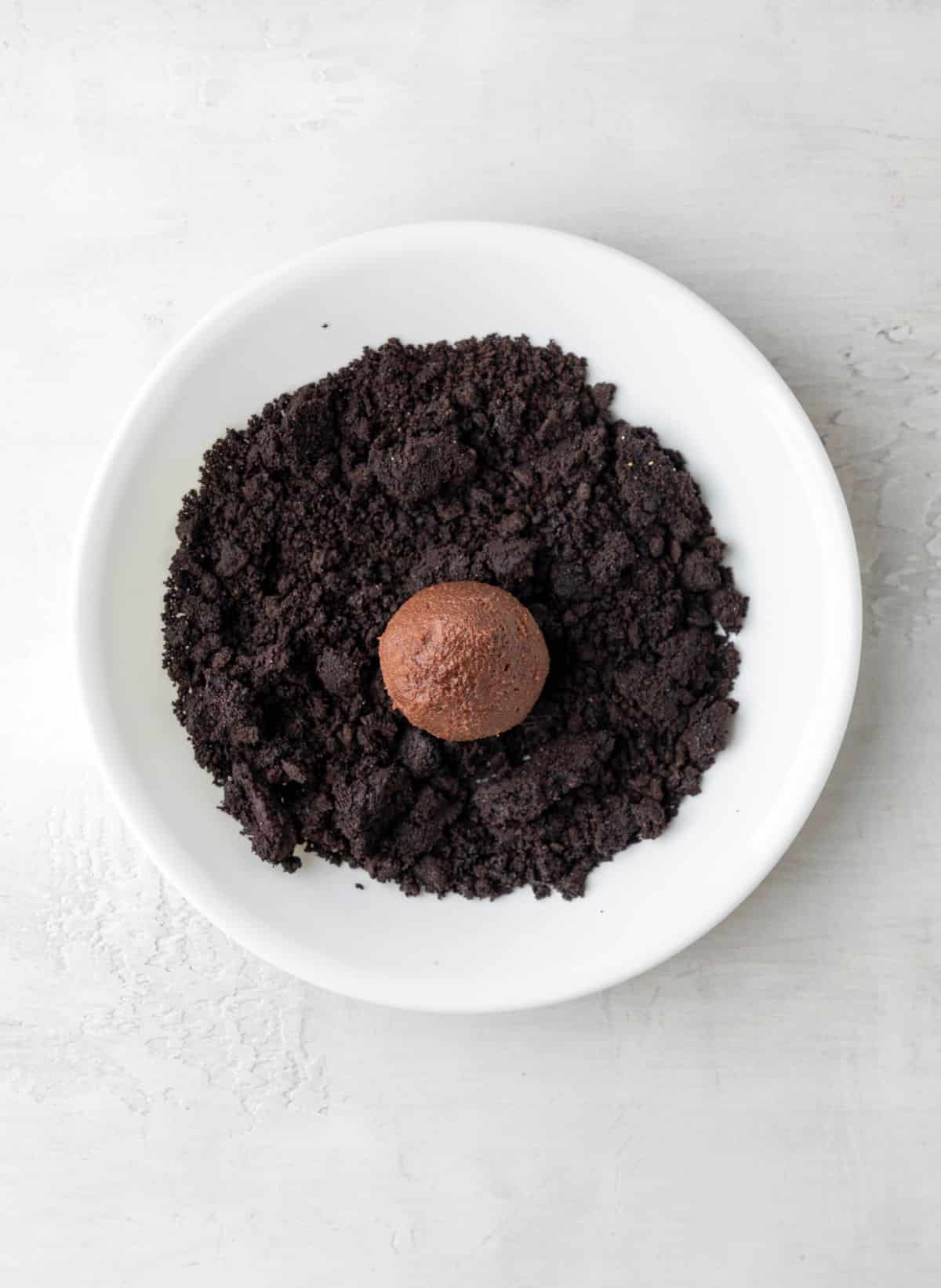 A cookie dough scoop in a dish of oreo cookie crumbs. 