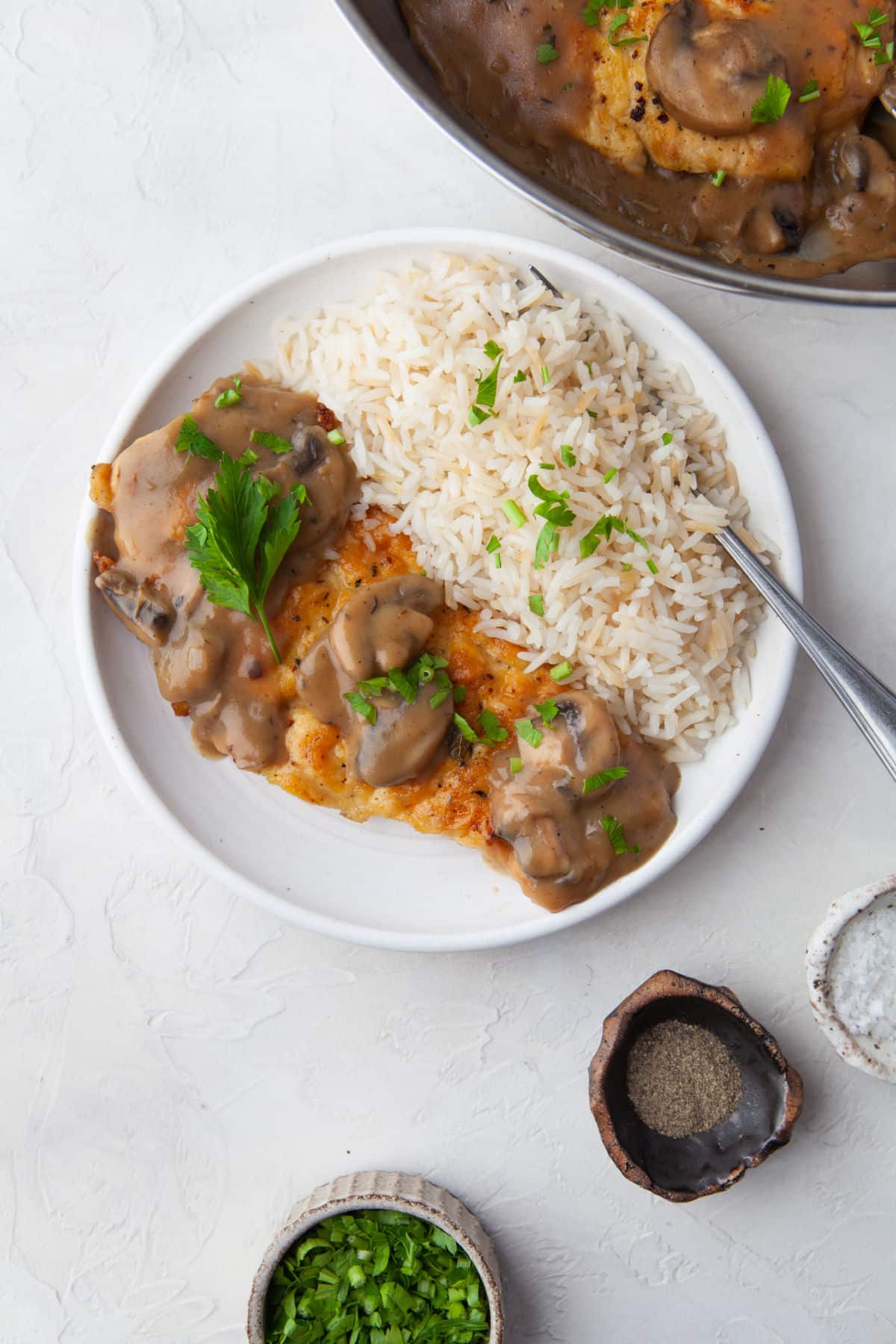 A white plate with chicken marsala and rice on it.