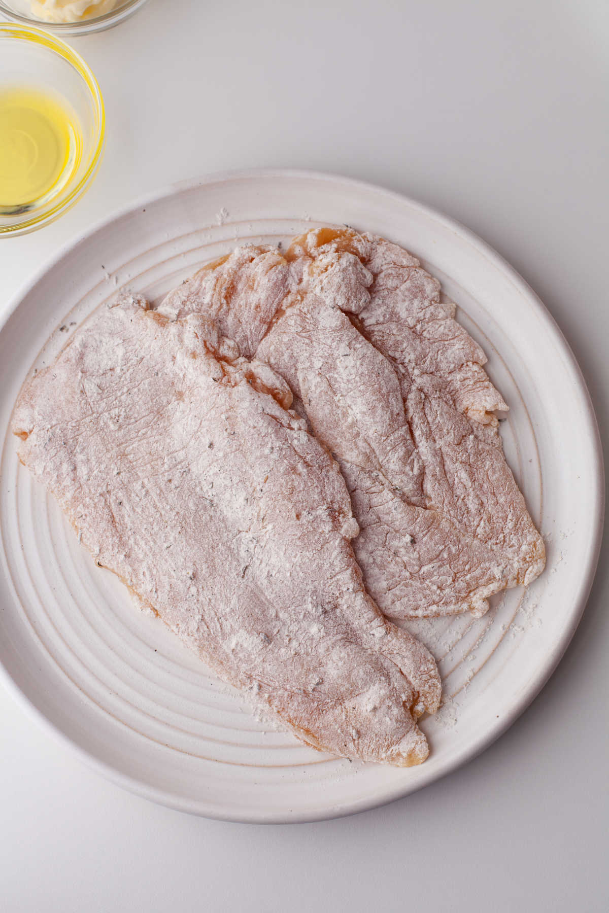 Flour coated chicken cutlets on a white plate. 