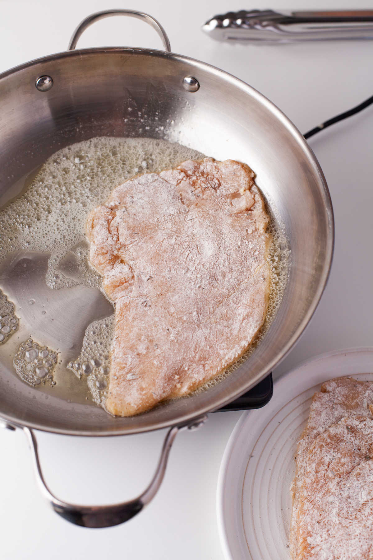 A flour coated chicken cutlet cooking in a pan.