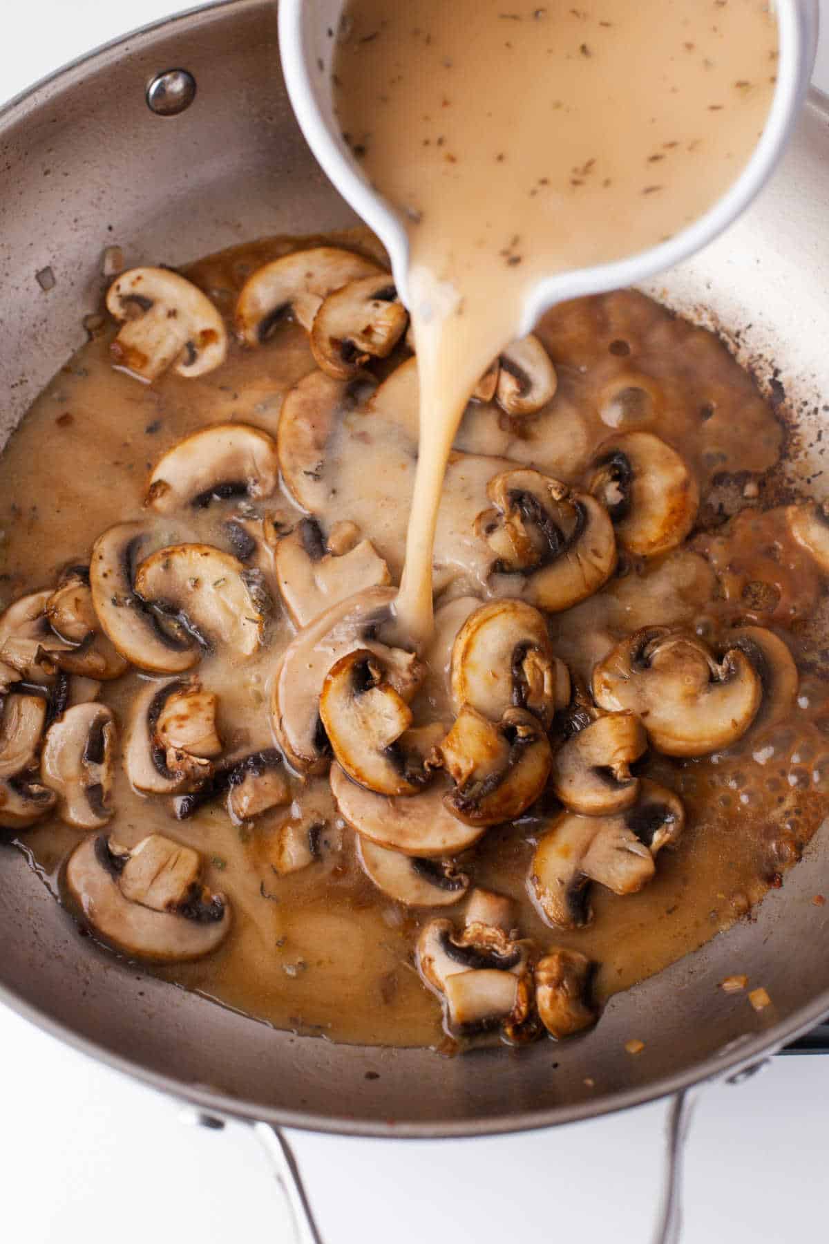 Marsala mixture pouring into mushrooms in a skillet. 
