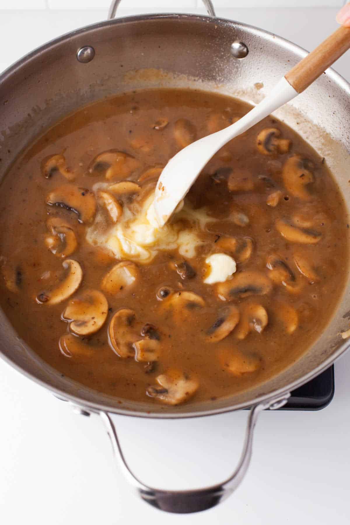 A spoon stirring butter into chicken marsala sauce. 