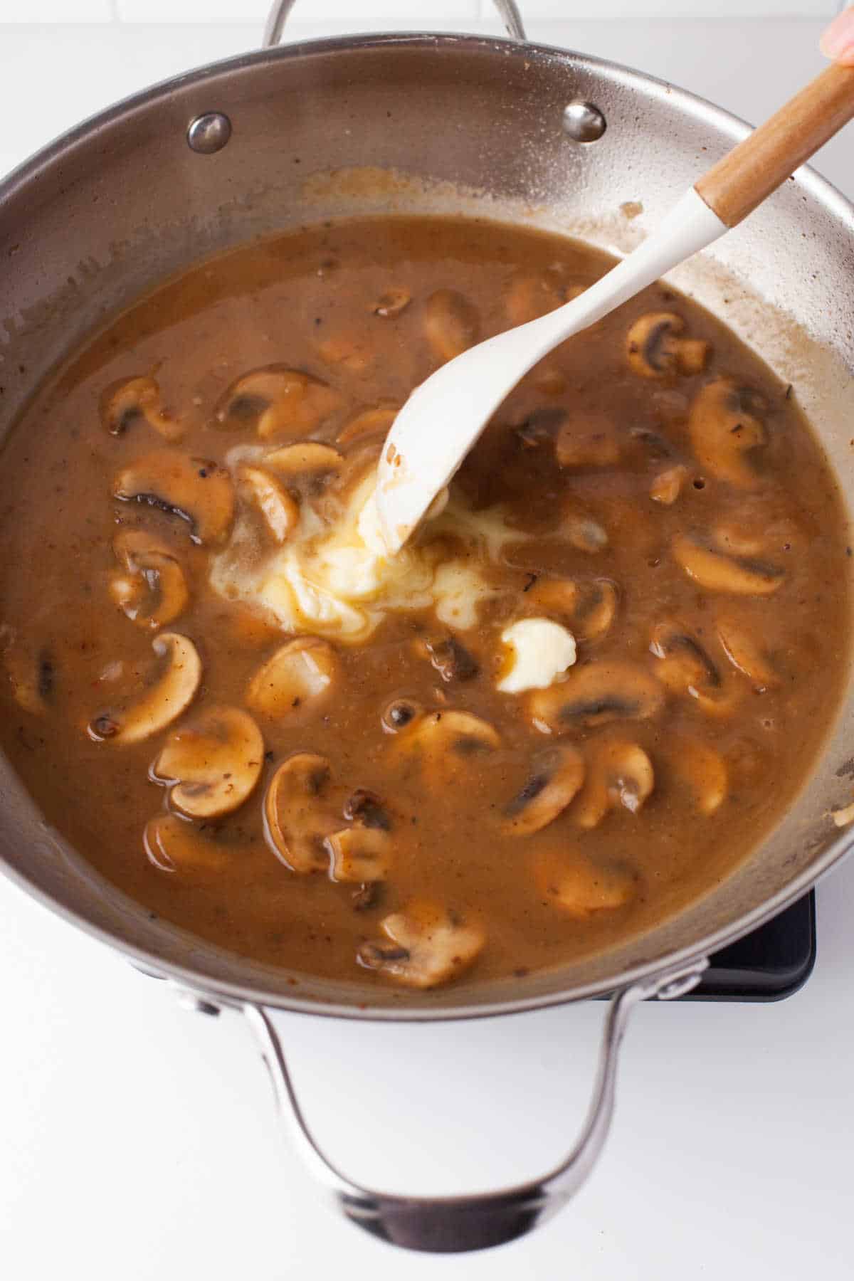 A spoon stirring butter into chicken marsala sauce.