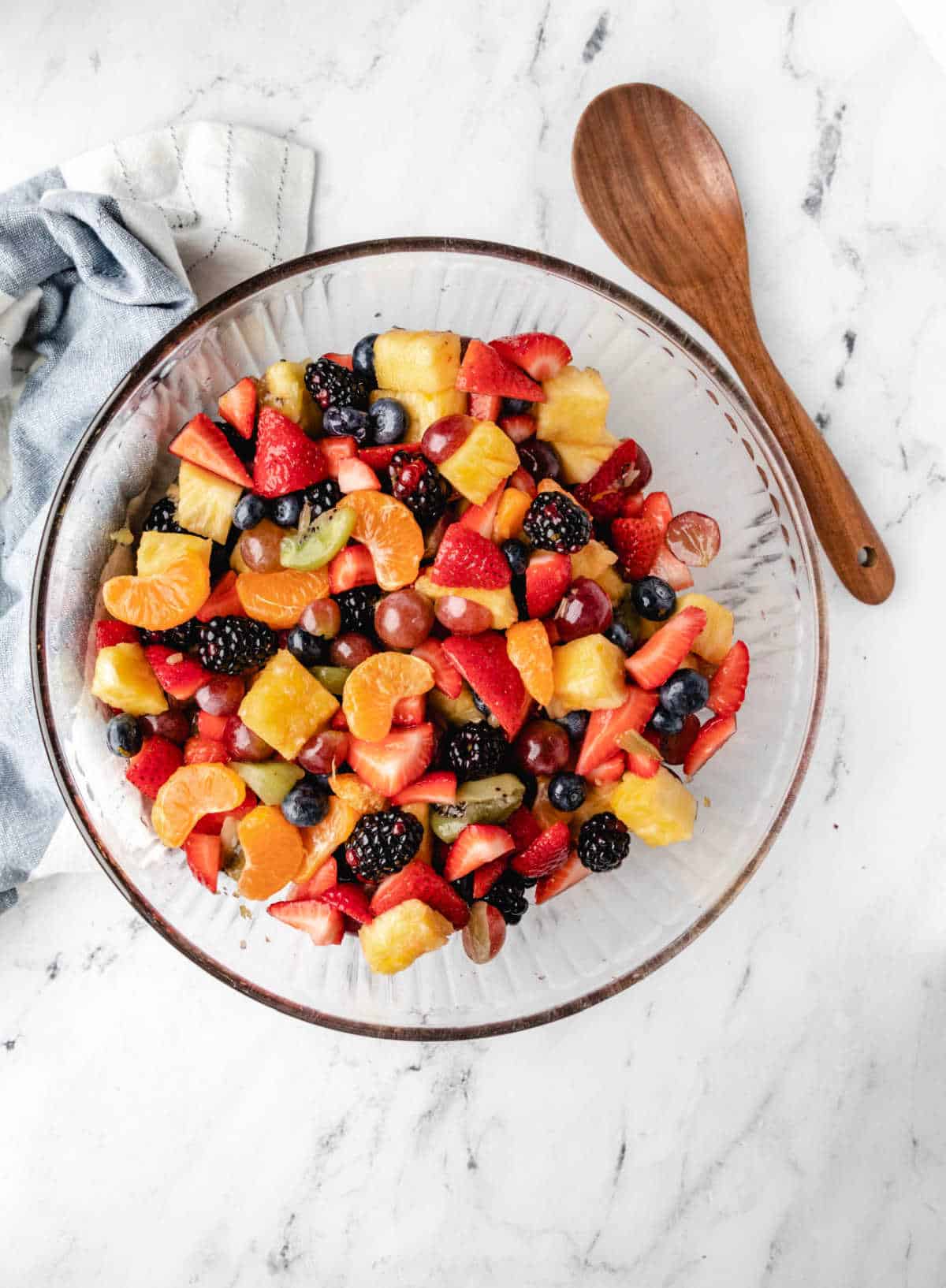 A bowl of fruit salad next to a wooden spoon.