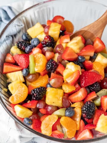 A wooden spoon in a glass mixing bowl full of fruit salad.