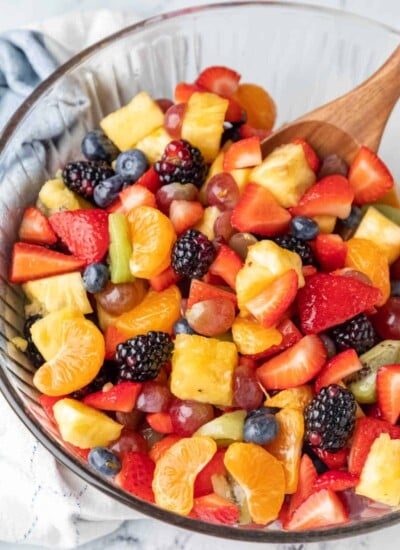 A wooden spoon in a glass mixing bowl full of fruit salad.