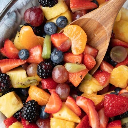 A wooden spoon scooping up fruit salad.