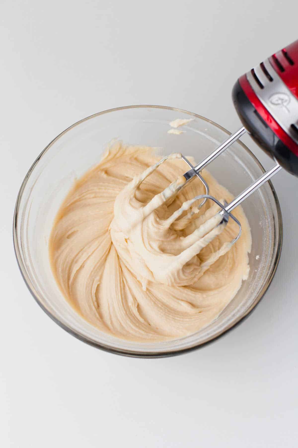 A hand mixer with its beaters in a bowl of salted caramel buttercream frosting.