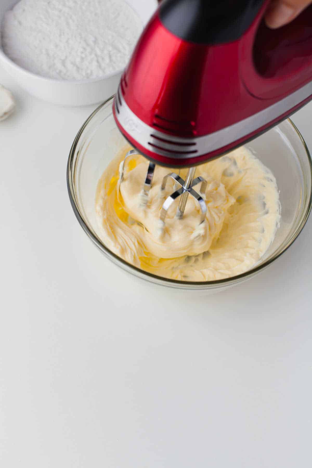 A hand mixer beating butter in a glass mixing bowl. 