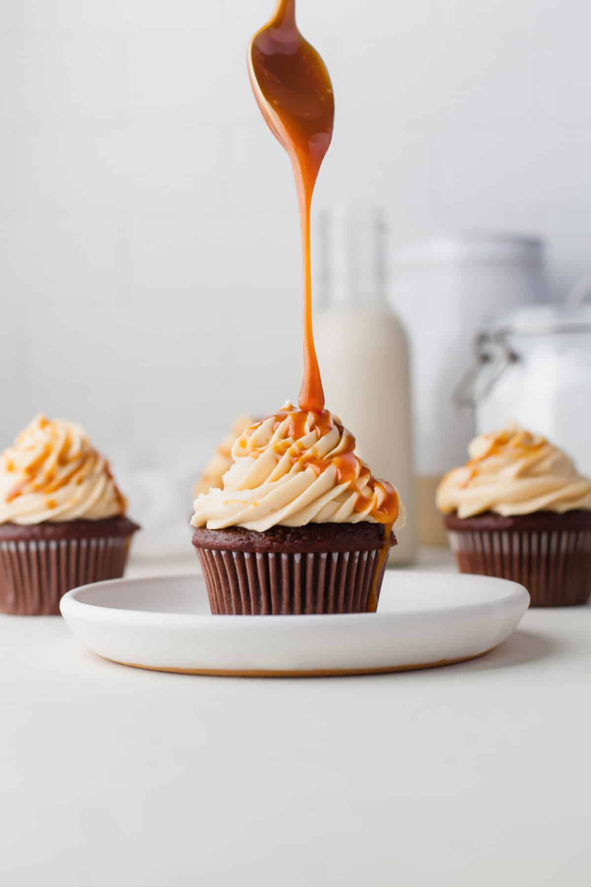 A spoon drizzling caramel sauce onto a cupcake topped with caramel frosting. 