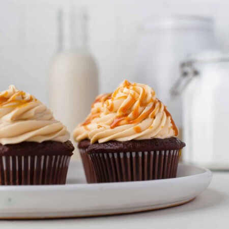A white plate with three chocolate cupcakes topped with salted caramel frosting.